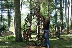 Jay leaning up against one of his sculptures with another sphere on top of it