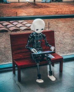 computer figure sitting on a bench with laptop on their lap
