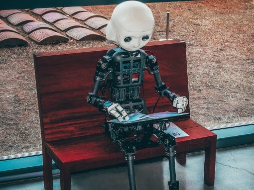 computer figure sitting on a bench with laptop on their lap
