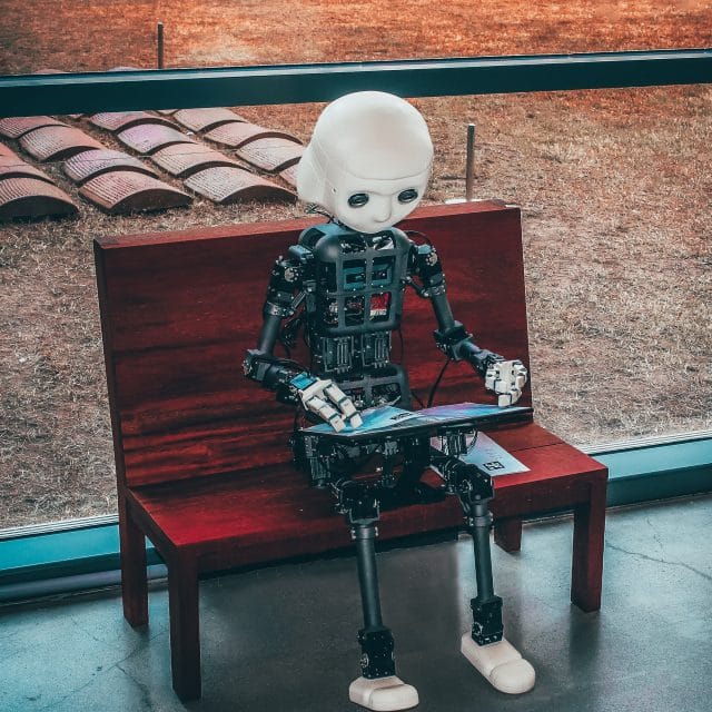 computer figure sitting on a bench with laptop on their lap